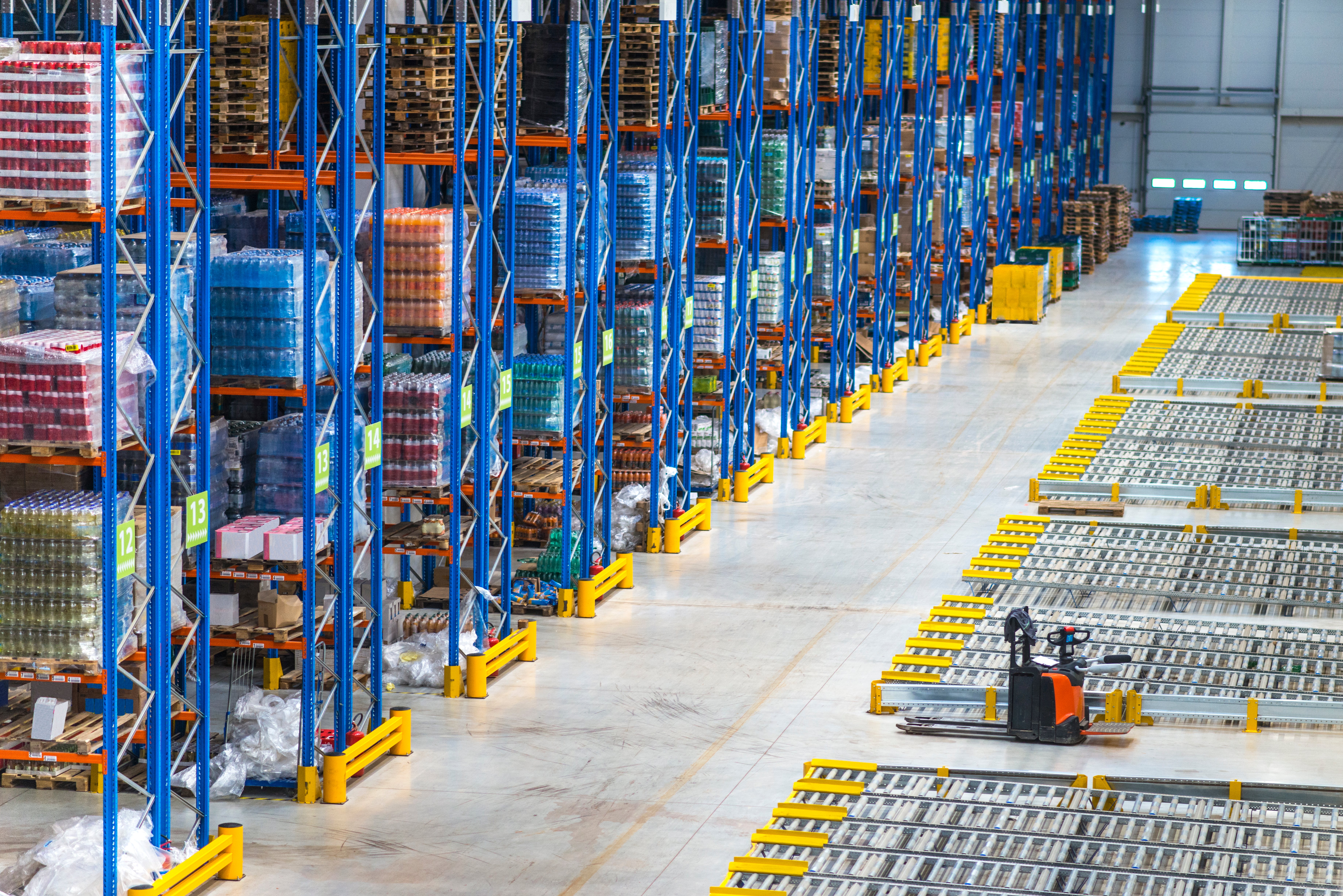 Interior of a large warehouse with tall blue pallet racking stacked with inventory and an orange pallet jack on the polished concrete floor.
