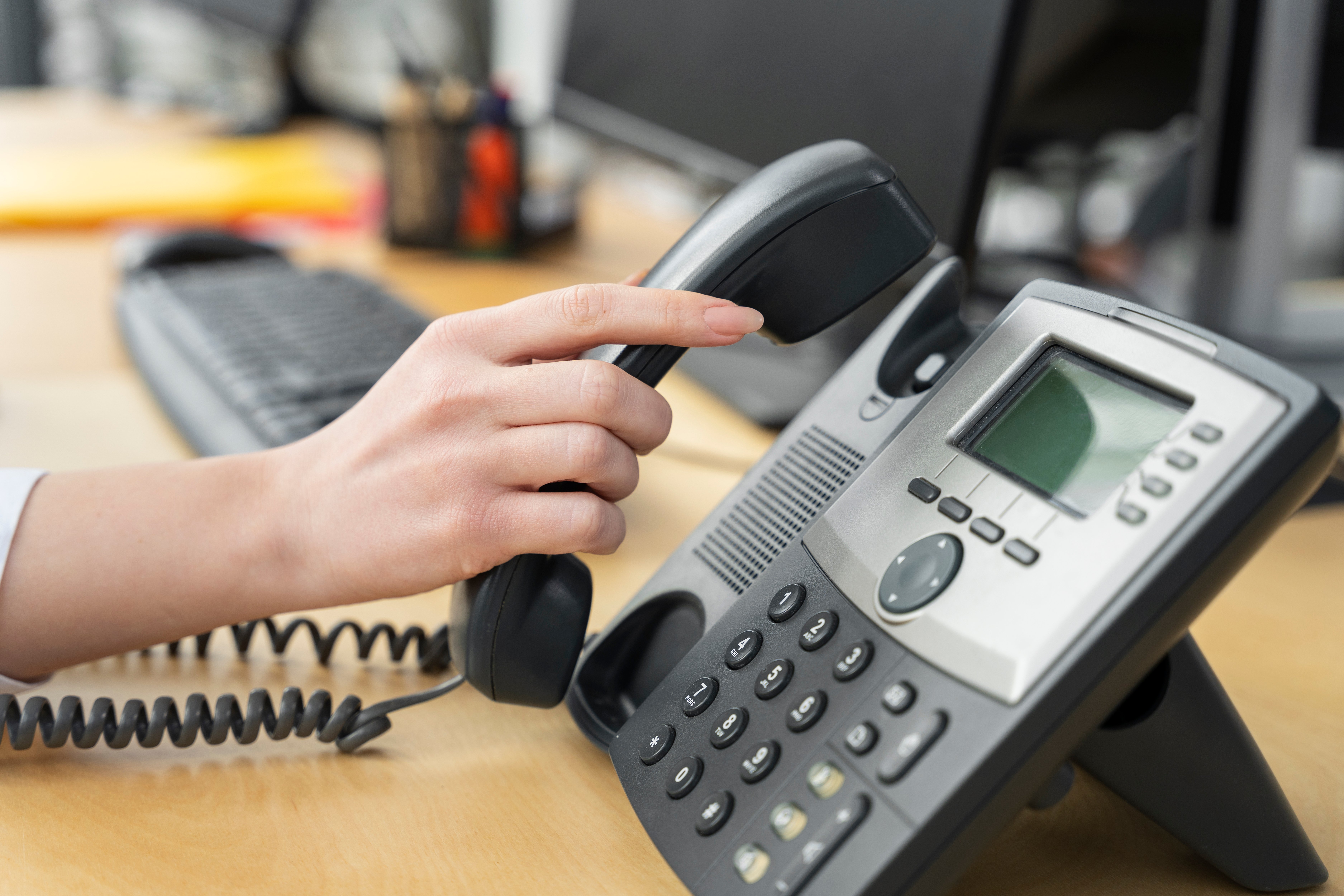 Close-up of a modern VoIP office phone with a person picking up the handset, representing the shift from POTS to internet-based phone systems.