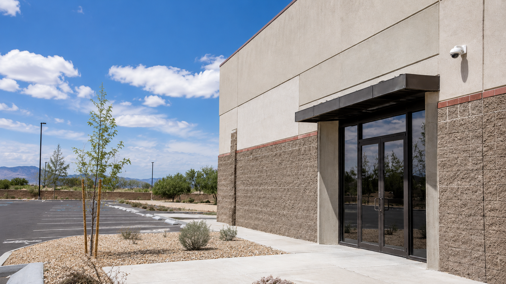 A vacant New Mexico commercial building with an empty parking lot and a dome security camera mounted by the entrance.